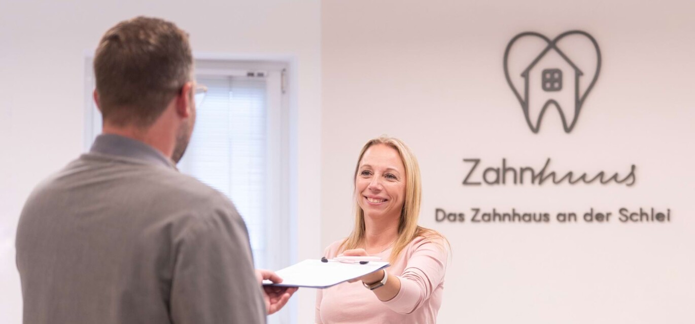 Freundliche Mitarbeiterin des Zahnhuus Kappeln begr&uuml;&szlig;t einen Patienten in der Praxis